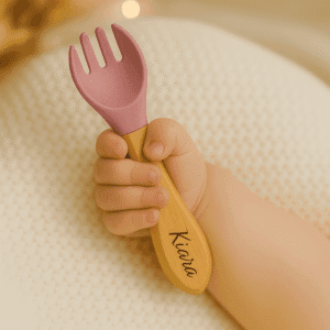 Fourchette bébé personnalisée avec prénom Kiara, manche en bois et embout en silicone vieux rose, tenue dans une petite main de bébé, idéale pour ses premiers repas. cadeau naissance, baptême, baby shower, anniversaire