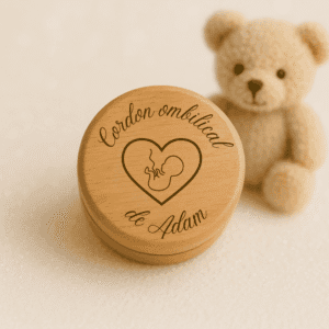 Boîte à cordon ombilical personnalisée en bois gravé avec le prénom Adam, posée sur un fond lumineux avec une peluche beige ourson en arrière-plan.
