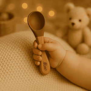 Cuillère bébé personnalisée avec prénom Nino, manche en bois et embout silicone marron, tenue dans la main d’un bébé, accessoire parfait pour les premiers repas. cadeau naissance, baptême, baby shower, anniversaire
