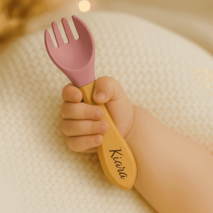 Fourchette bébé personnalisée avec prénom Kiara, manche en bois et embout en silicone vieux rose, tenue dans une petite main de bébé, idéale pour ses premiers repas. cadeau naissance, baptême, baby shower, anniversaire